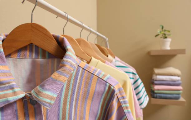 Wooden hangers with stylish clothes on rack near beige wall. Dressing room interior
